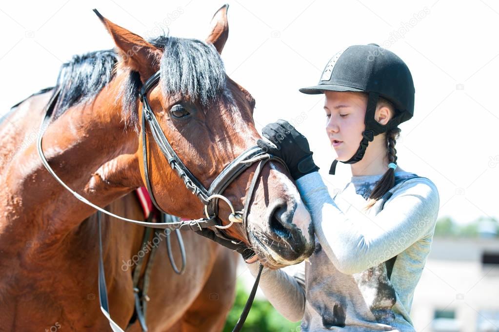 Young teenage girl owner harnessing bay stallion for training