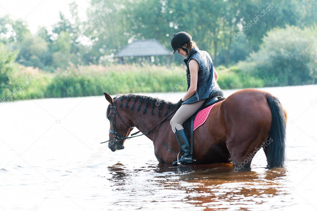 Young teenage girl riding horseback in river at early morning