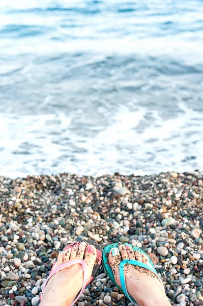 Summertime relaxation on pebble sea coast. Woman feet in slipper — Stock Photo, Image