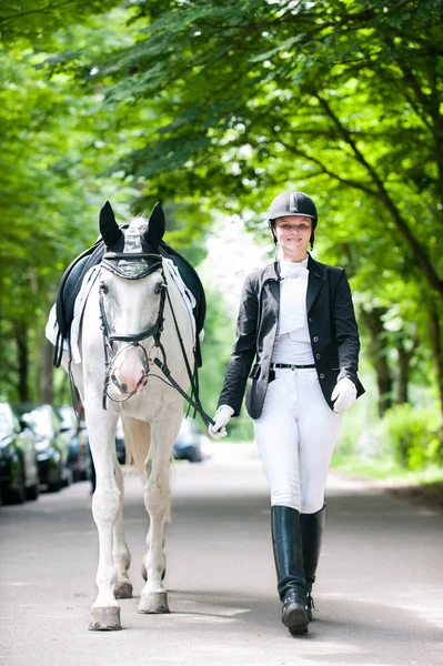 Smiling pretty teenage girl leading white horse at competition — Stock Photo, Image