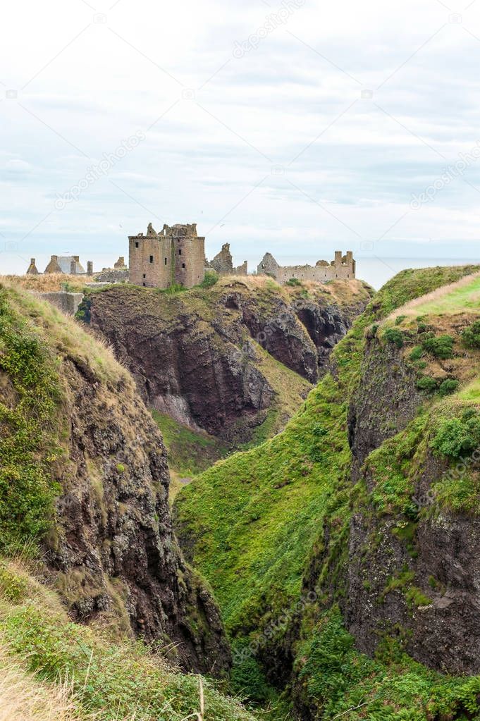 Ruins of ancient Dunnottar castle in green scottish hills.