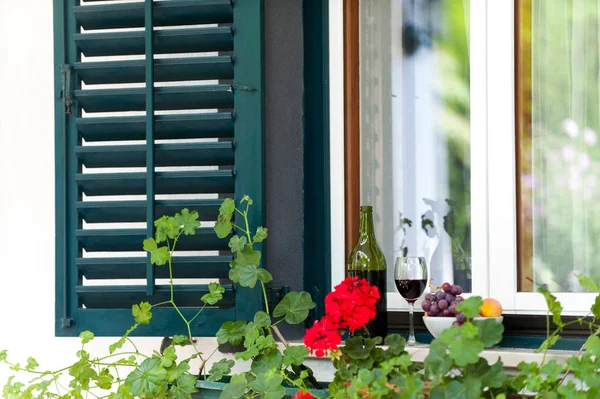 Copo com vinho tinto e alguma uva na borda da janela — Fotografia de Stock