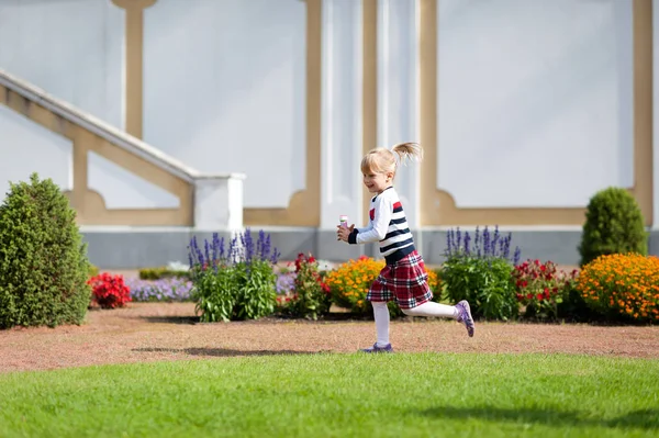 Fröhliches kleines blondes Mädchen spielt im sommergrünen Park — Stockfoto
