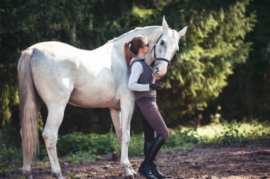 Genç ve neşeli bayan koçun portresi en sevdiği beyaz ata içtenlikle sarılıyor. Filtreli renkli açık hava yatay yaz dönemi görüntüsü