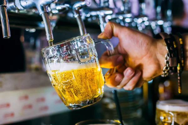 Biranın döküldüğü fincanı tutarken. Barmen bardağa bira doldurur..