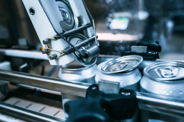 The process of closing beer cans on the conveyor. An automatic machine rolls up the lids on the beer cans.