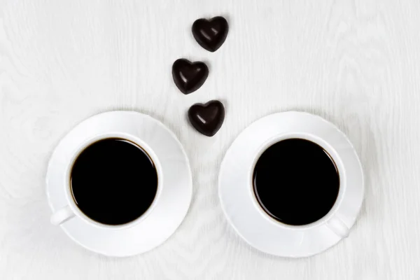 Dos tazas blancas de café en la mesa blanca con corazones de bombones —  Fotos de Stock