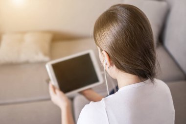 Yatağın üzerinde tablet üzerinde çalışan genç bir kız. Karantina anlamında uzaklık öğrenimi, kişisel eğitim