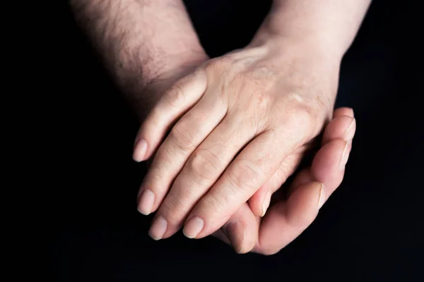 Hands of seniors men and women on a black paper background Hand of men touching senior women.