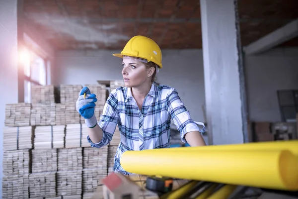 Sarı şapka takan kadın inşaat mühendisi, yenileme evinde bina planı üzerinde çalışıyor.
