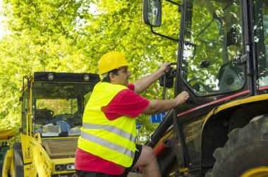Yol işçisi yol makinesinde sarı üniformalı ve kasklı bir kapı açıyor. mMan bir inşaat alanı aracında çalışacak