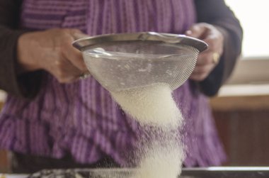 Kadın flor ya da şeker tozunu süzer. Tatlı için hazırlık malzemesi. Mutfakta elek elek, yakın.