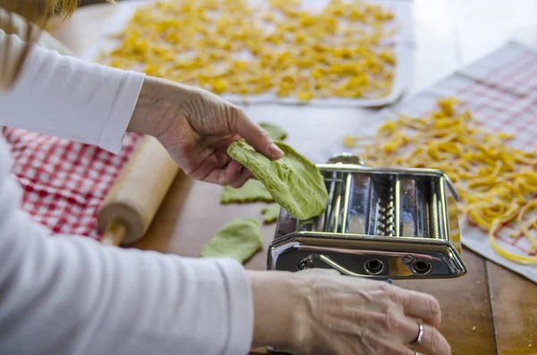 Preparing pasta tagliatelle on handy machine. Woman make fresh noodle from green dough with spinach.Domestic food