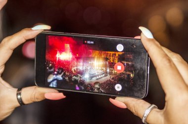 Kadın yılbaşı ışıklarıyla akıllı telefonun fotoğrafını çekiyor.