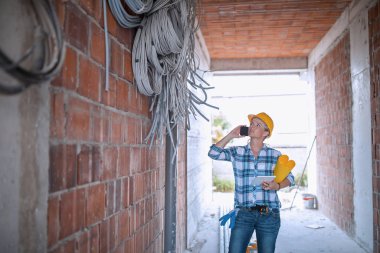 İnşaat alanında çalışan kadın elektrik işçisi elektrik kablolarını kontrol ediyor. İnşaat teftişinde çalışan yakışıklı kadın mühendis.