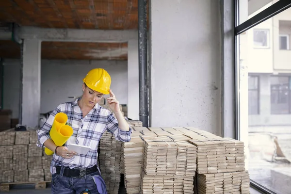 Exhausted architect with helmet on construction site indoor.Female civil engineer controlling material for renovating house