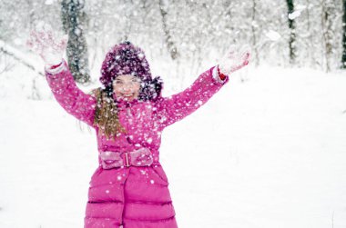 Parkta karla kaplı ağaçları olan şapkalı mutlu küçük kız.