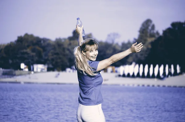 Young woman cheerful jump on the beach holding bottle of fresh w — 스톡 사진