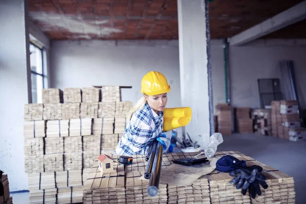 Exhausted architect with helmet on construction site indoor. Female civil engineer controlling material for renovating house