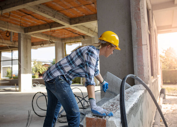 Женщина-работница осваивает металлические сетки на бетонных стенах. Красивая гражданка-инженер работает на стройплощадке.
