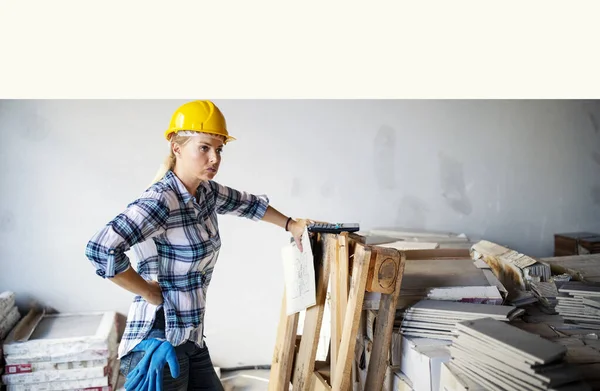Exhausted architect with helmet on construction site indoor.Female civil engineer controlling material for renovating house