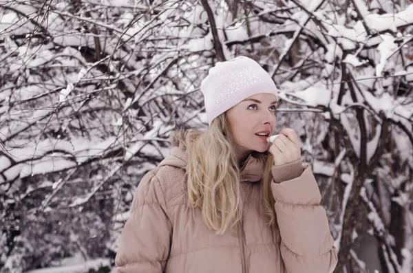 Pretty girl applying lip balm on cold winter day outdoor. Nordic woman in warm clothes putting cosmetic protection for lips on snowy season