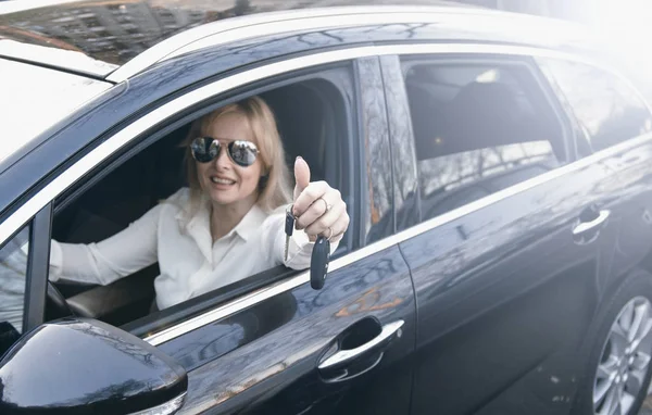 車のキーを手に若い女性の運転席に座って オープンウィンドウを通して笑顔 車をレンタルし または購入する満足したビジネス女性 — ストック写真
