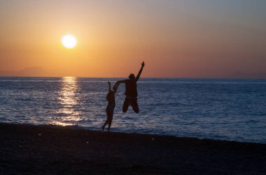 Mutlu genç bir kadın gün batımında denize atlıyor, seyahat ediyor ve tatile çıkıyor.