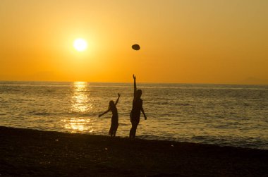 Gün batımında sahilde zıplayan bir kadının silueti.