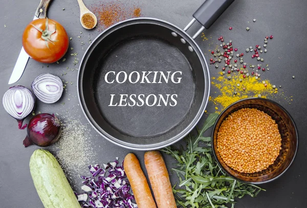 Sebzeler, baharatlar ve kızartma tavası. Düz siyah masa üzerinde daha az pişen harflerle. Üst görünüm aşçılık dersleri konsepti..