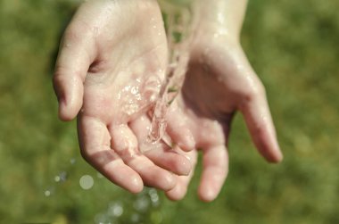 Close up on child hand catching water. Splashing drops on sunny summer outdoor background. Environment and health concept. Flowing clear cool Drink Selective focus kid hand taking water.