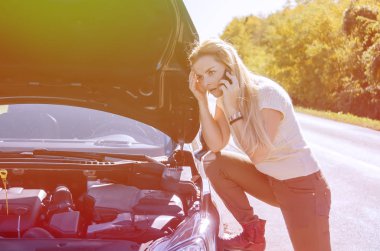 Yoldaki bozuk arabanın yanında duran kadın sürücü, çekici servisini arıyor. Genç sarışın kadın, araba yolculuğunda sorun yaşıyor, cep telefonunu yardım için kullanıyor.