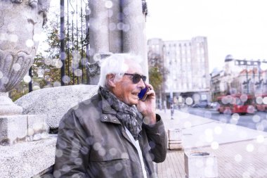 Şehir sokaklarında akıllı telefon kullanan şık, yaşlı ve yakışıklı bir adam. Mutlu yaşlı, yakışıklı, gri saçlı adam cep telefonuyla konuşuyor.