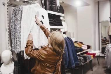 Butikte son sınıf kadın kıyafetleri. Olgun kadın tasarımcı alışveriş merkezinde indirimli kıyafet seçer.