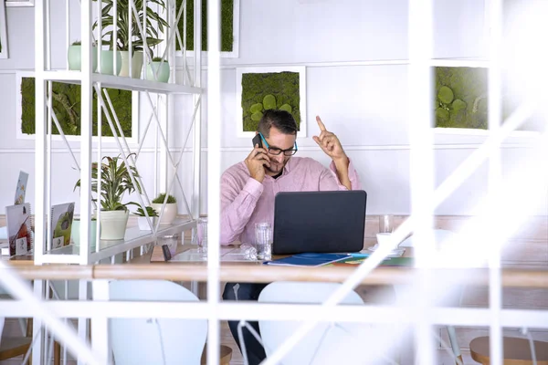 Young handsome man working in coffee bar on his laptop, reading paper document.Busy man productivity on job using internet wifi