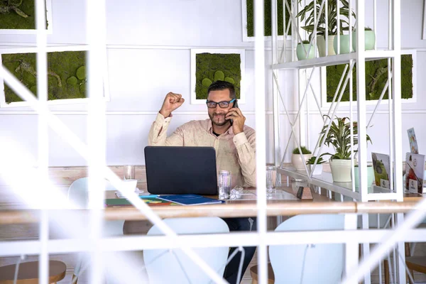 Young handsome man working in coffee bar on his laptop, reading paper document.Busy man productivity on job using internet wifi