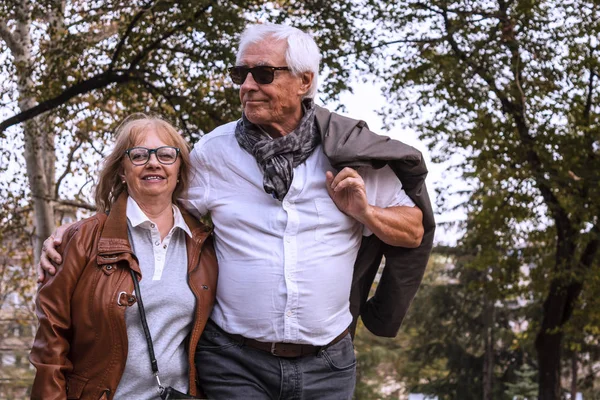Happy old couple in walk outdoors. Senior man and wife hugging and walking. Active seniors in autumn park