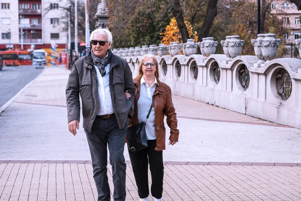 Dışarıda yürüyen mutlu yaşlı çift. Kıdemli karı koca sarılıp yürüyorlar. Sonbahar parkında aktif yaşlılar