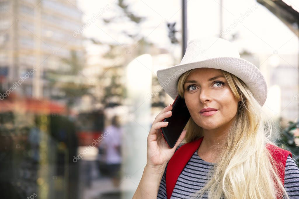 Woman in urban city street using smartphone.Young blonde long hair female using mobile phone in town. Copy space