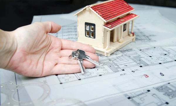 Woman finger with keys of new house. House model on architectural project paper with keys of new home. Investment for vacant house. Deposit credit in bank.