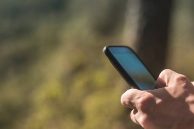 Ormanda cep telefonu kullanan bir kadının ellerine yakın çekim.