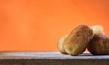 Beyaz tabakta turuncu arka planı olan tavuk kroketleri.