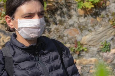 Virüs salgını sırasında yüzünde koruyucu maske olan bir kadın sağa bakıyor..