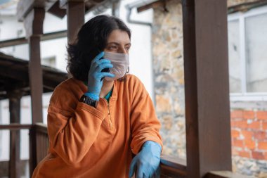 Hava kirliliği ya da virüs koronavirüsü salgını nedeniyle mavi cerrahi maske takan bir kadın telefonda konuşuyor..