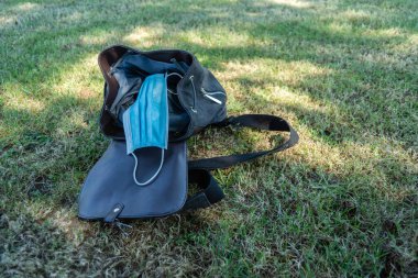 Yeşil çimen zemininde siyah sırt çantalı mavi cerrahi maskeler. Covid19 virüs konsepti