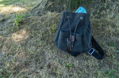 Yeşil çimen zemininde siyah sırt çantalı mavi cerrahi maskeler. Covid19 virüs konsepti