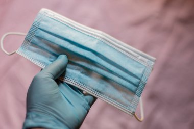 Plastik eldivenli bir el pembe arka planda virüs koruması için yüz maskesi takıyor. Covid19 virüs konsepti.