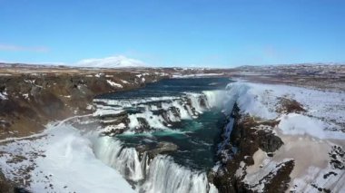 İzlanda. Kışın Gullfoss Şelalesi. 4K Video İHA kullanıyor. Yukarıdan bakınca, turkuaz suyu görmenizi sağlıyor. Ayrıca, uzaktaki buzulu ve mavi gökyüzünü görebilirsiniz..