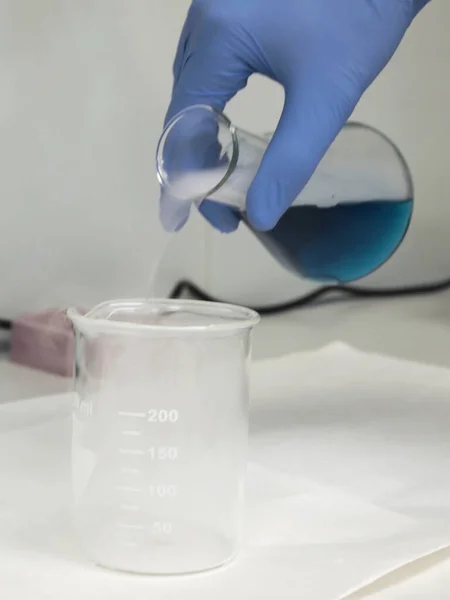 Flacon met een blauwe vloeistof en droog ijs dat in een bekerglas wordt gegoten — Stockfoto
