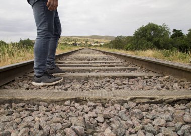 Bulutlu bir günde, kırsal bir bölgede tren raylarında duran tanınmayan genç adam.